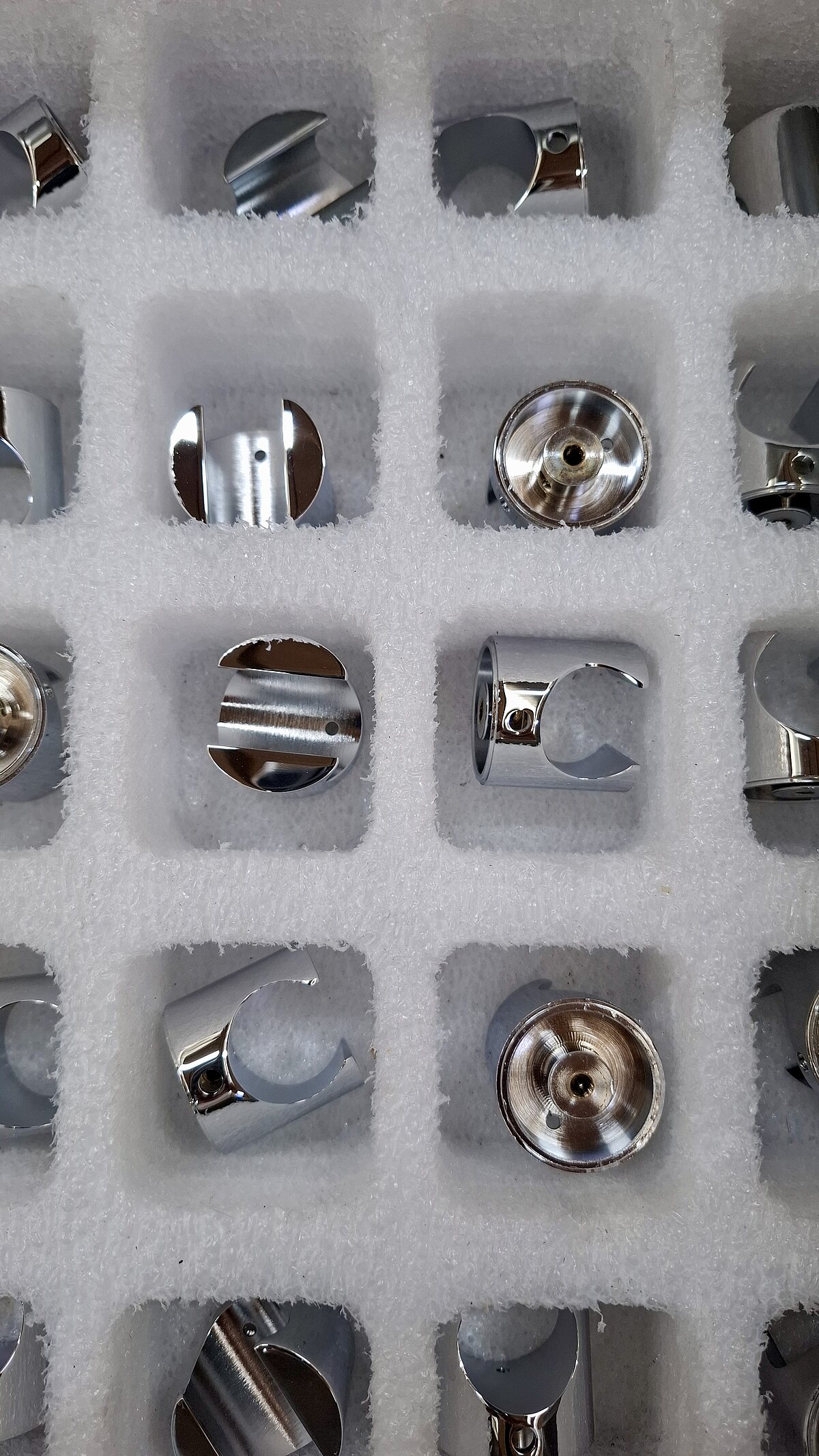Mehrere glänzende Metallteile in einer Schaumstoffverpackung mit einzelnen Fächern.