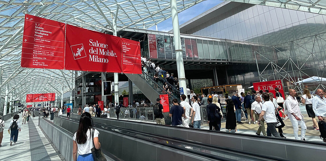 Eine Menschenmenge in warmer Kleidung hat sich auf einer verschneiten Straße in der Nähe eines Gebäudes versammelt. Zu sehen sind festliche Dekorationen.