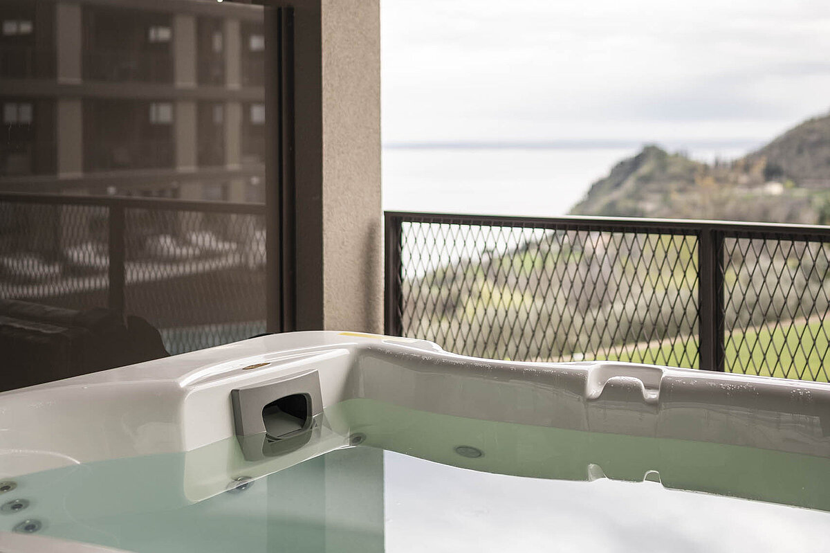 Ein Whirlpool auf einem Balkon mit Blick auf das Meer und eine hügelige Landschaft im Hintergrund. Der Himmel ist bewölkt.