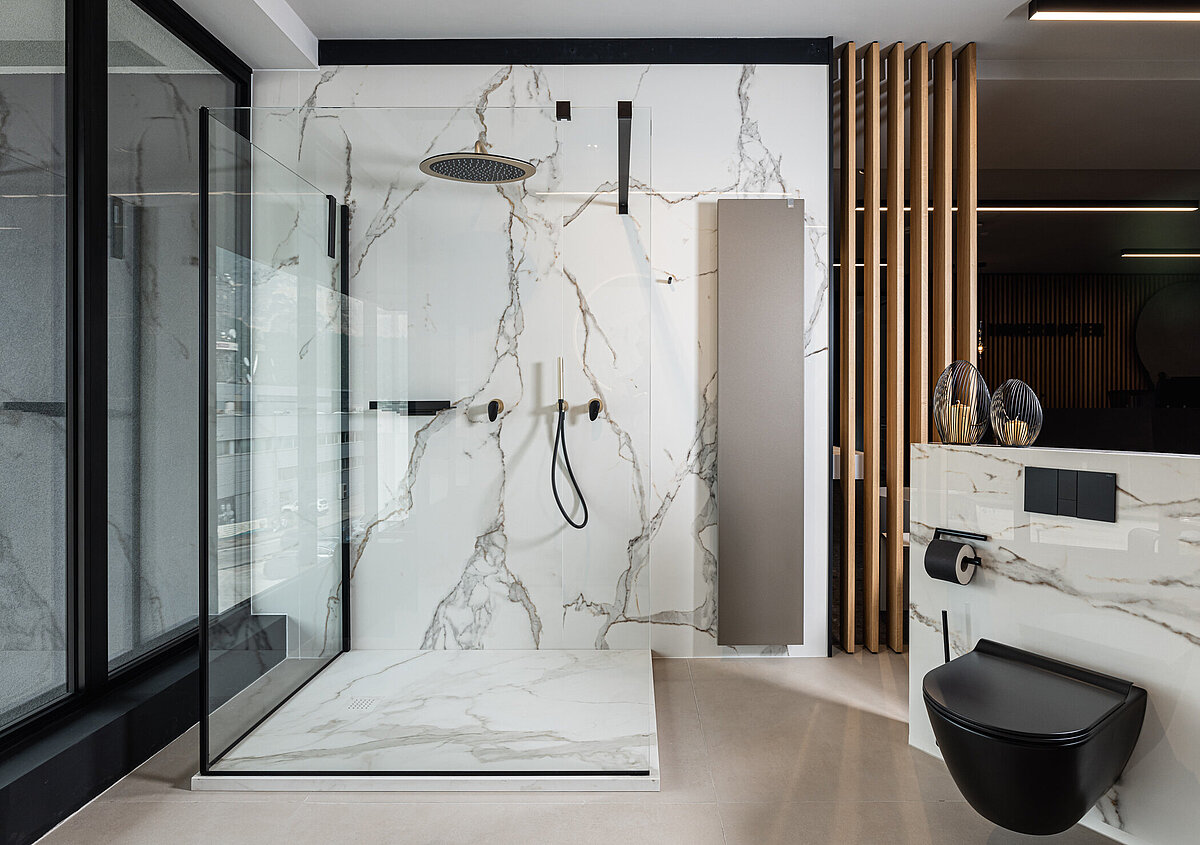 Modernes Badezimmer mit Marmormuster, großer verglaster Dusche und Regendusche. Eine schwarze Toilette und stilvolle Dekorationen vervollständigen das elegante Design. Hölzerne Akzente trennen die Bereiche und bieten eine warme Atmosphäre. Große Fenster bringen viel Licht herein.