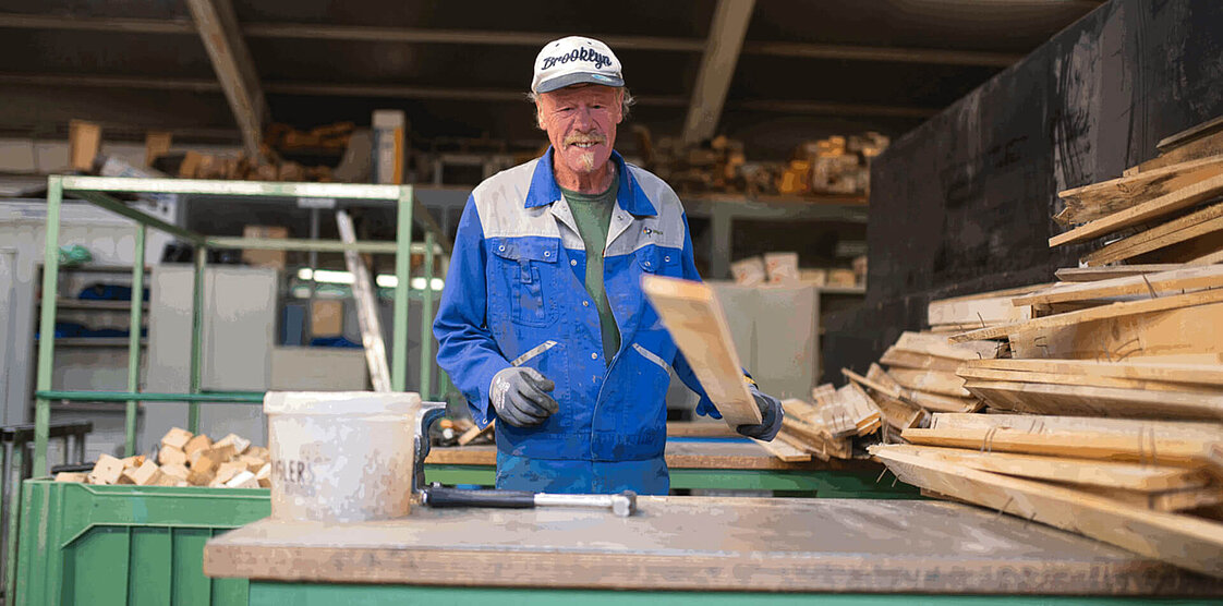 Arbeiter in blauer Uniform und Helm steht in einer Industrieanlage mit Bedienfeldern und großen Säcken im Hintergrund.