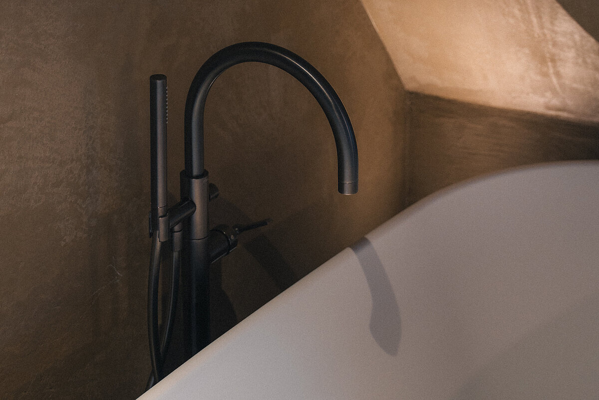 Moderne Badewanne in einem minimalistischen Badezimmer mit matt-schwarzem Wasserhahn und einer Wand mit sanfter Beleuchtung.