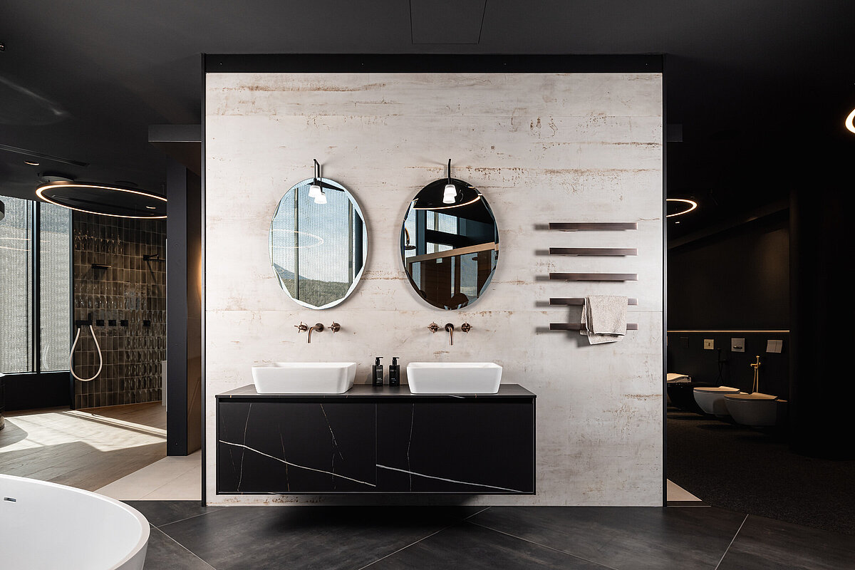 Modernes Badezimmer mit zwei runden Spiegeln über einem Doppelwaschbecken mit Marmoroptik. Minimalistisches Design mit dunklen Farbtönen. Wand aus hellem Holz und schwarze Schränke.
