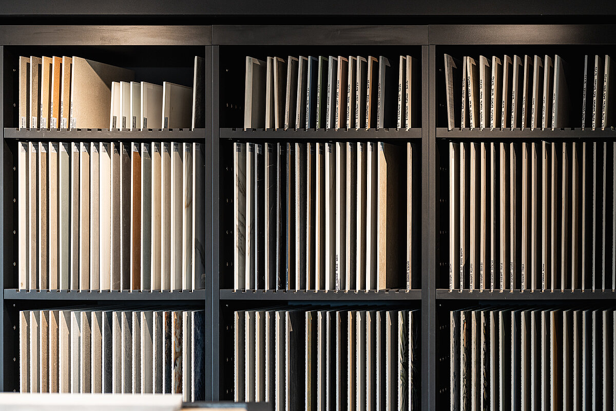 Ein dunkles Bücherregal voller gleichmäßig aufgereihter Bücher und Ordner, die aufrecht stehen. Die Bücher und Ordner sind ordentlich sortiert und haben meist einen hellen oder neutralen Einband. Das Regal ist gleichmäßig beleuchtet.