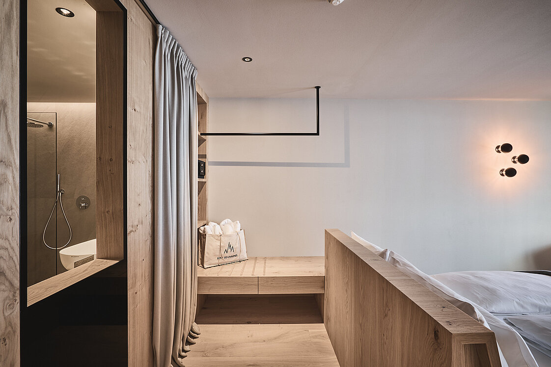 Moderne Küchentheke mit einer weißen Schüssel, einer Topfpflanze, einem kleinen schwarzen Gerät und Küchenutensilien auf einer hellen Holzoberfläche. Auf einem Regal darüber stehen ein paar Gläser und Behälter.