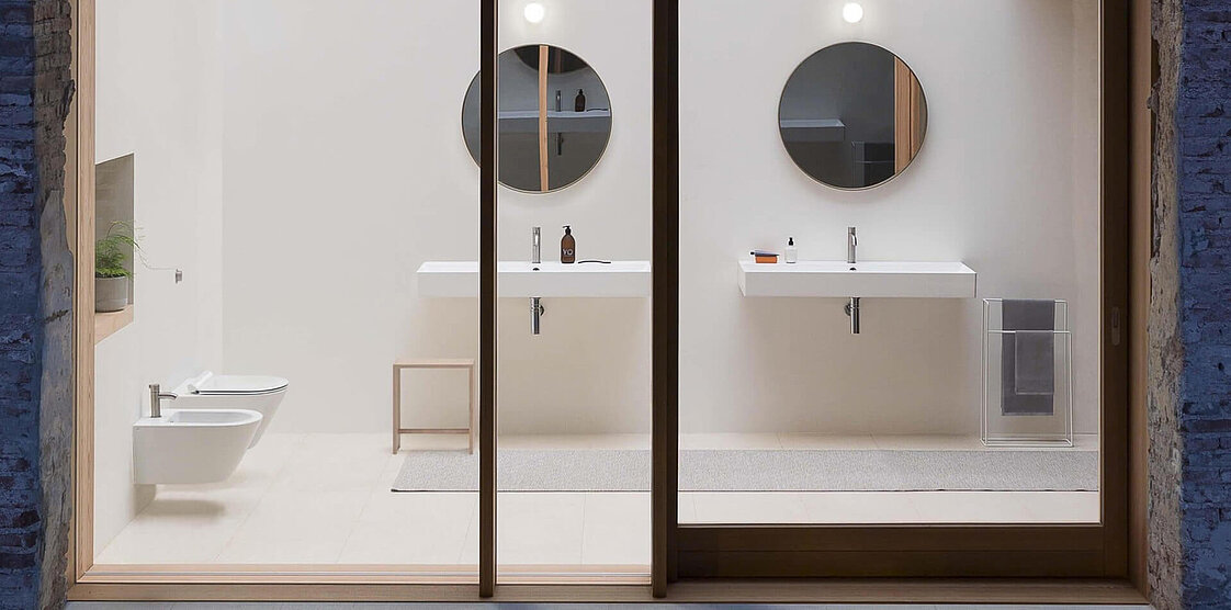 Modernes Badezimmer mit zwei Waschbecken, runden Spiegeln und beigen Ablagen.