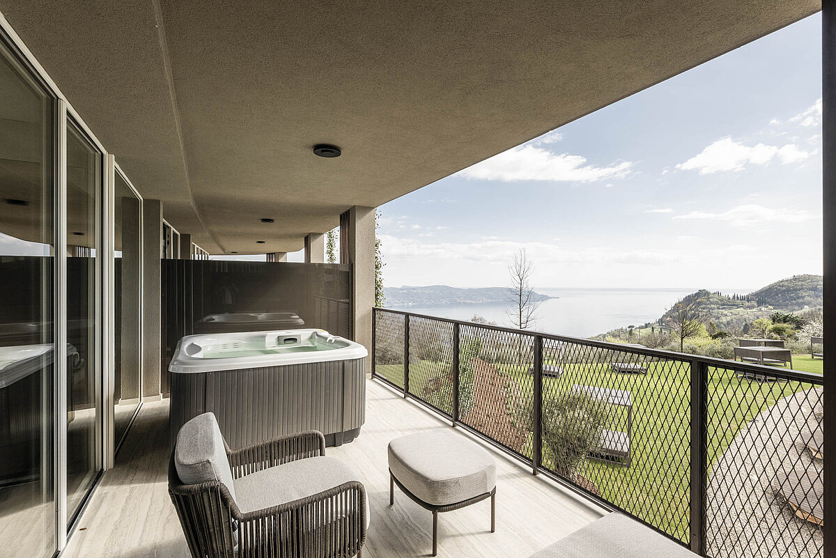Terrasse mit Whirlpool und zwei bequemen Sesseln, mit Blick auf eine weite Landschaft und ein entferntes Gewässer.